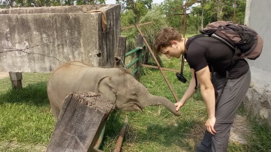 Ein junger Mann in Wanderklamotten und ein kleiner Elefant